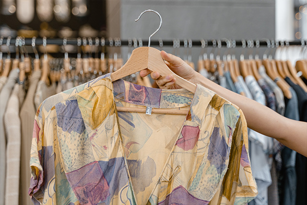 Hand holding a coat hanger with a blouse in a retail environment with blurred backgrond